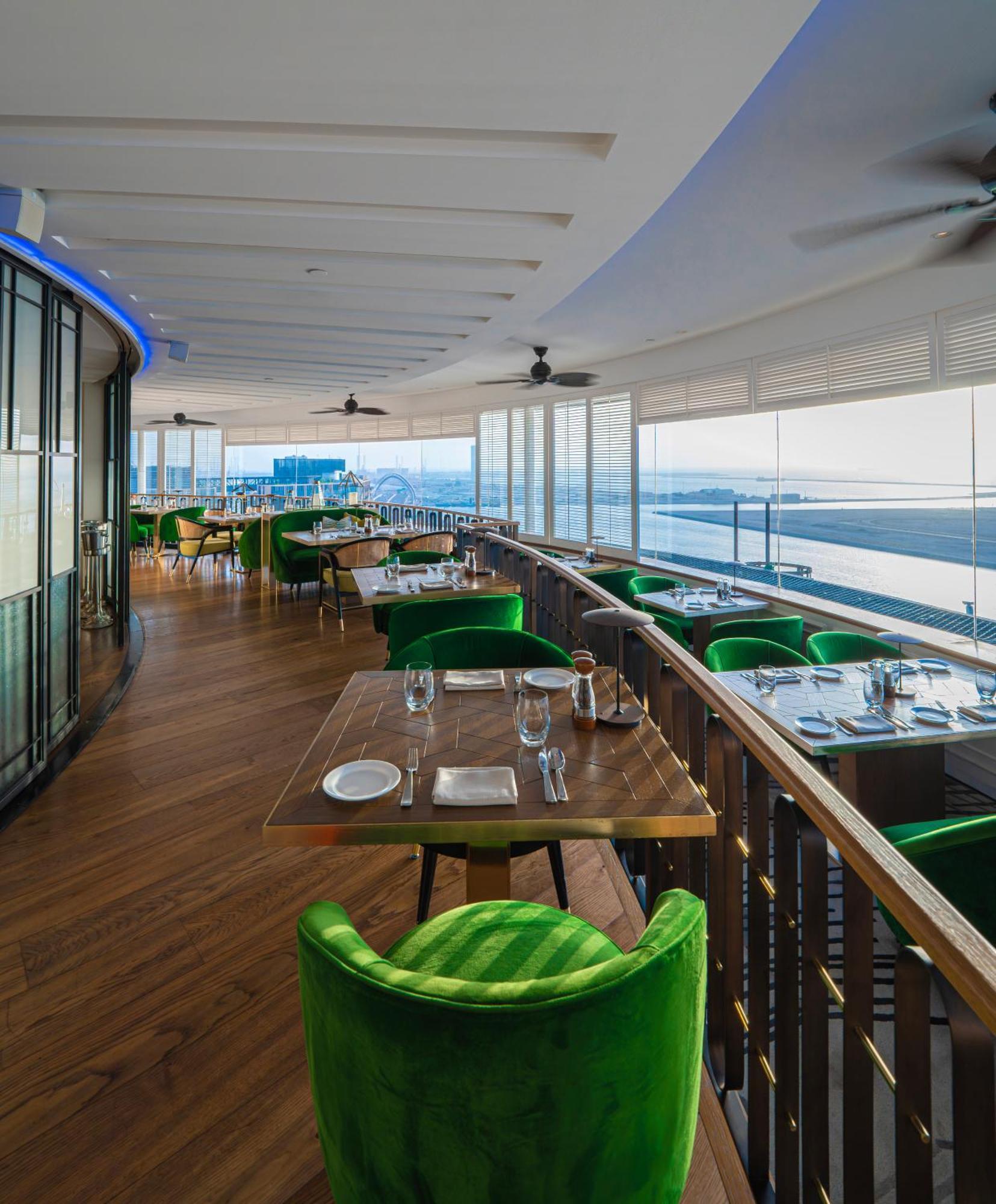 Hotel Hyatt Regency Dubai - Corniche Esterno foto The photo shows a stylish restaurant interior with a modern design. It features several tables set for dining, each adorned with plates, glasses, and silverware. The chairs are upholstered in vibrant green fabric, adding a pop of color to the space. 